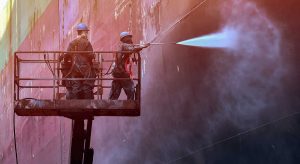 workers cleaning the exterior of the ship with water blast