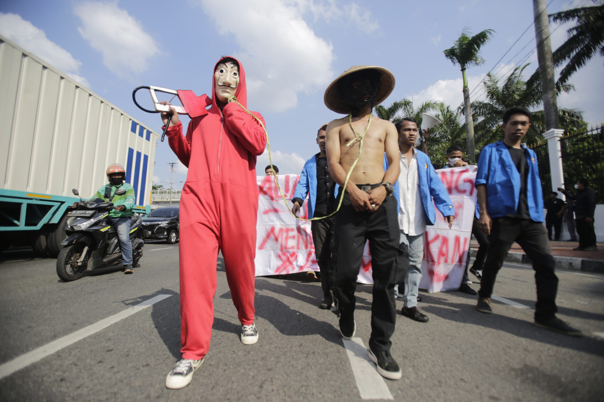 Student demonstrators depicting fuel mafia and victim chained on his neck, walking down the street. Indonesia