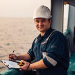 Deck Officer on deck of offshore vessel or ship , wearing PPE personal protective equipment. He fills checklist. Paperwork at sea