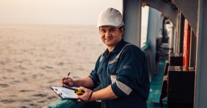 Deck Officer on deck of offshore vessel or ship , wearing PPE personal protective equipment. He fills checklist. Paperwork at sea