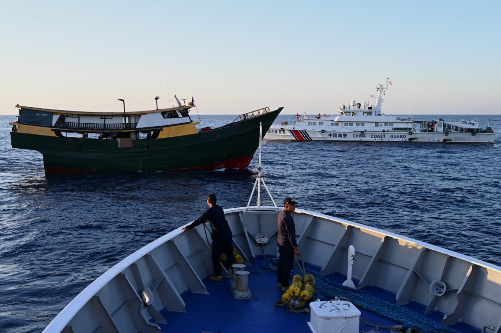 A China Coast Guard (CCG) vessel (right, rear) sails on March 5, 2024 in the disputed South China Sea near the Unaizah May 4 (midground), a ship chartered by the Philippines&rsquo; military for a resupply mission to Second Thomas Shoal.