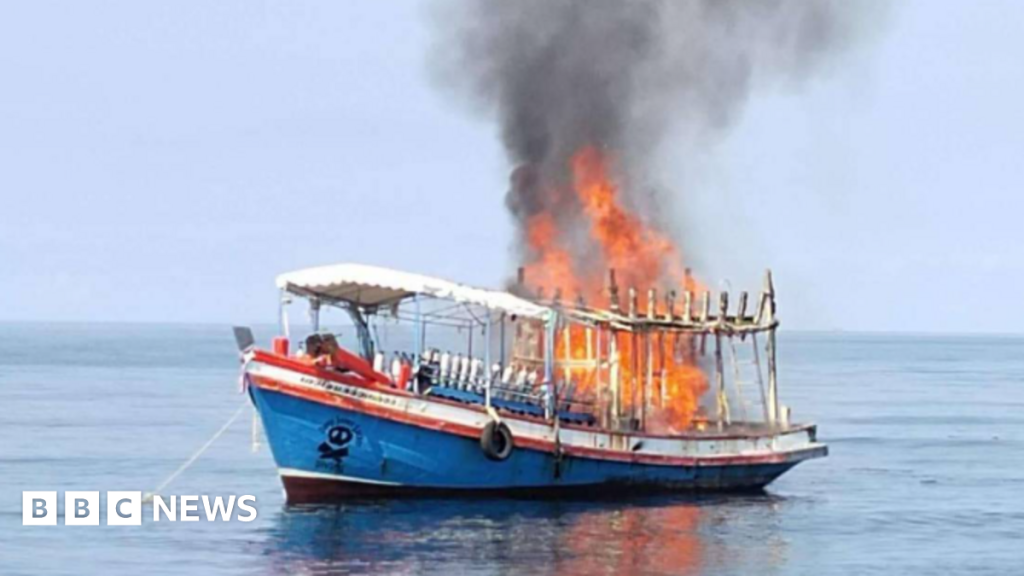 Tall orange flames rise into the sky on a small red, white and blue boat in the water off Koh Tao